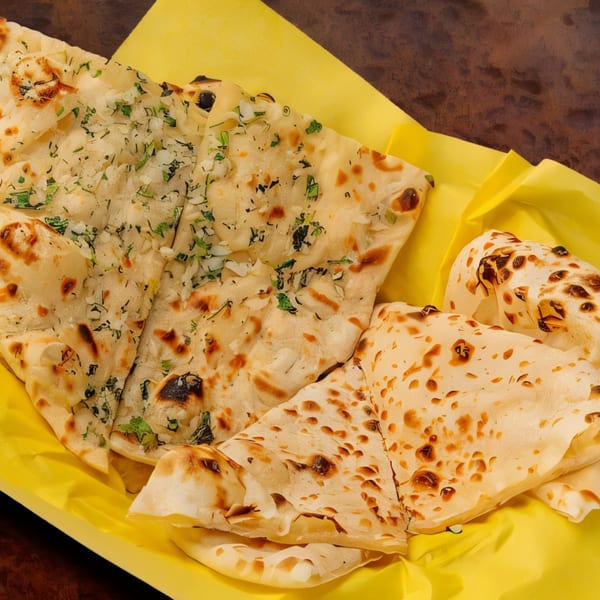 Freshly baked Indian naan bread, some with herbs, served in a yellow basket.