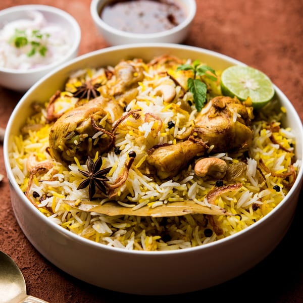 A bowl of India House On Wheels chicken biryani with rice, cashews, and spices, garnished with mint and lime.