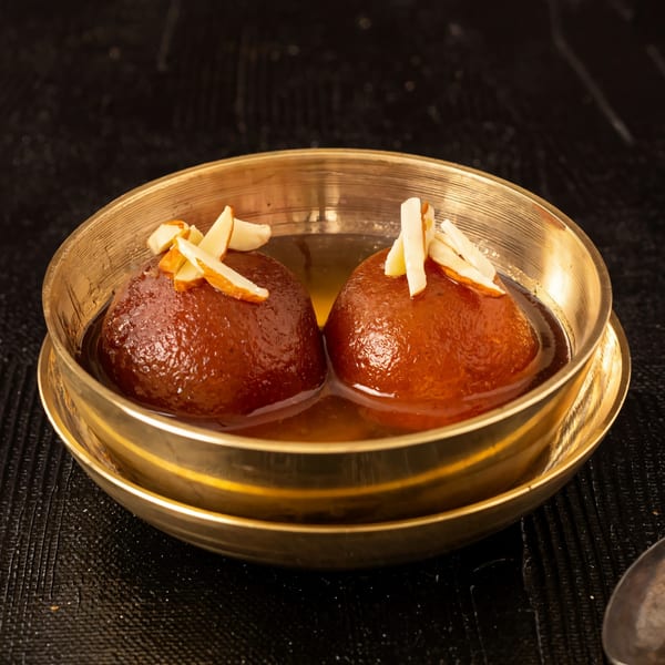 Two gulab jamun, Indian fried dough balls in syrup, topped with sliced almonds in a brass bowl.
